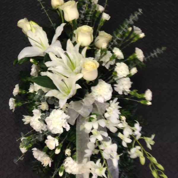 White floral spray with lilies, roses, and orchids on a dark background