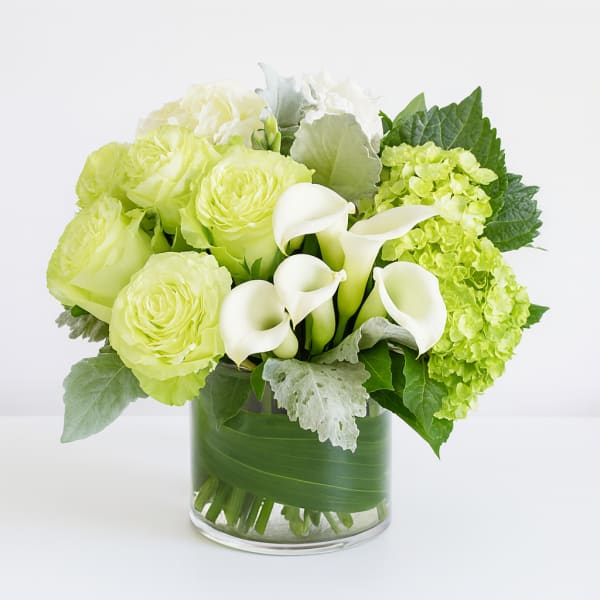Green and white bouquet with calla lilies and roses in a glass vase