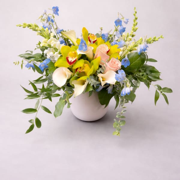 Mixed bouquet in a white vase with yellow, blue, peach, and white flowers