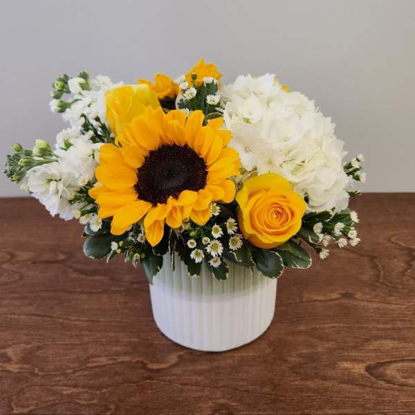Yellow sunflower and rose arrangement in a white vase with white blooms