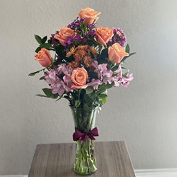 Tall bouquet of peach roses and purple flowers in a clear glass vase