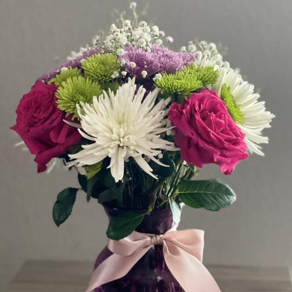 Pink roses and white chrysanthemums in a purple vase with a ribbon