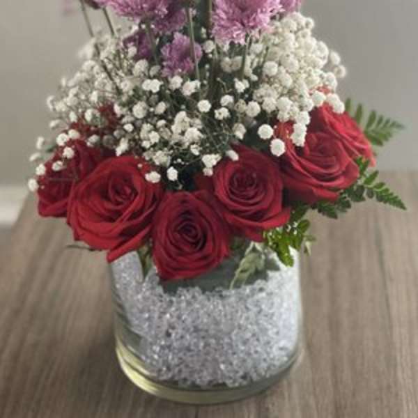 Red roses and purple flowers arranged in a glass vase