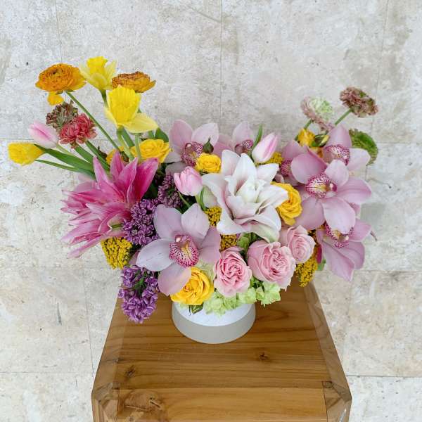 Mixed bouquet of pink, yellow, and white flowers in a round white box