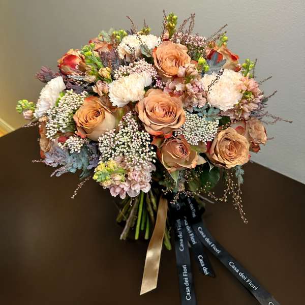 Peach roses and white blooms arranged in a hand-tied bouquet