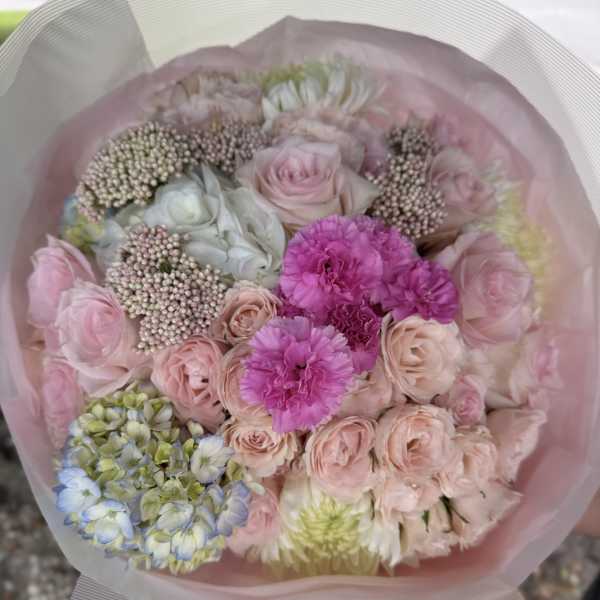 Pastel bouquet of pink roses, carnations, and hydrangea wrapped in pink paper