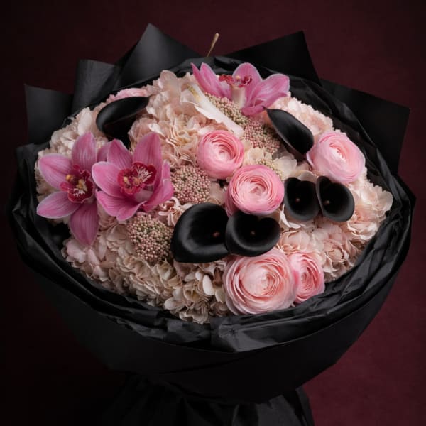 Pink bouquet with orchids, ranunculus, and pale hydrangeas wrapped in black paper