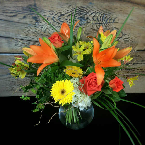 Bouquet of orange lilies, red roses, and yellow daisies in a glass vase