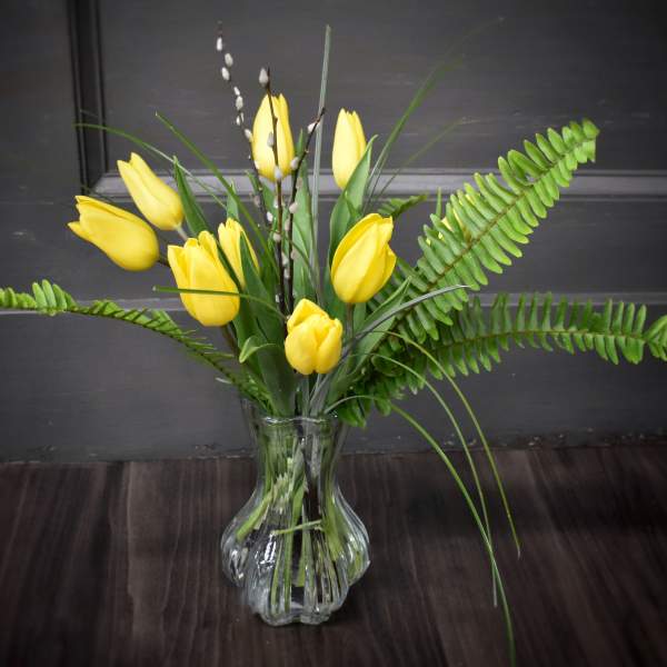 Yellow tulips arranged in a clear glass vase with fern fronds