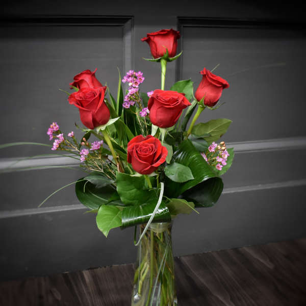 Red roses with small purple filler flowers in a clear glass vase