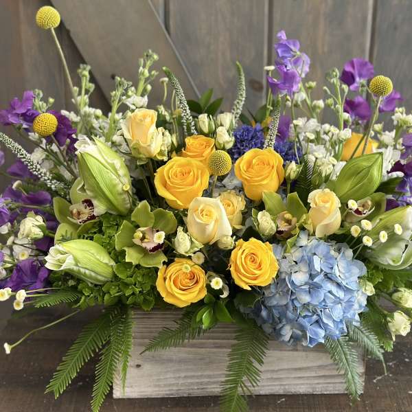 Mixed bouquet with yellow roses, purple flowers, and blue hydrangea in a wooden box