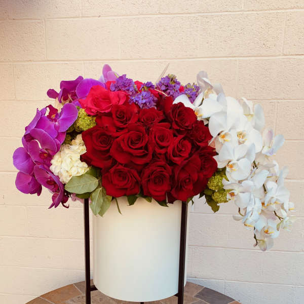 Large floral arrangement of red roses, purple orchids, and white orchids in a tall stand