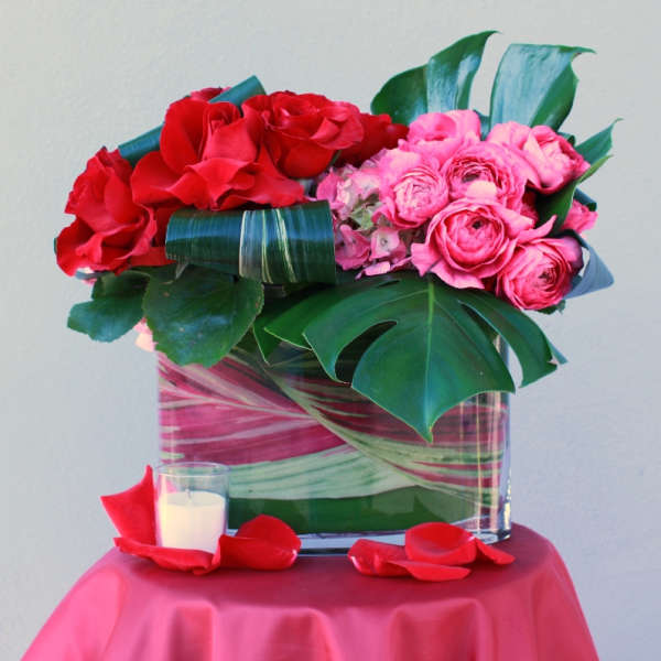 Red and pink rose arrangement in a glass vase with a candle