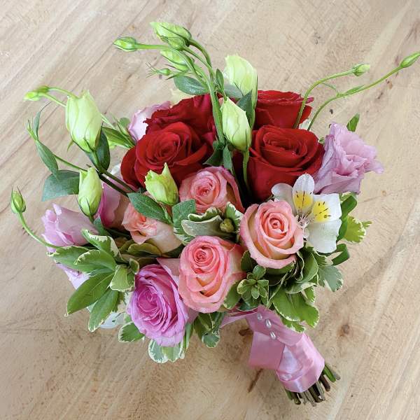 Hand-tied bouquet of red and pink roses with white blooms and ribbon