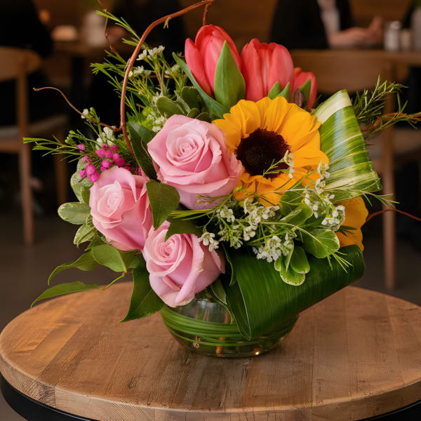Pink roses and a sunflower arranged in a glass vase