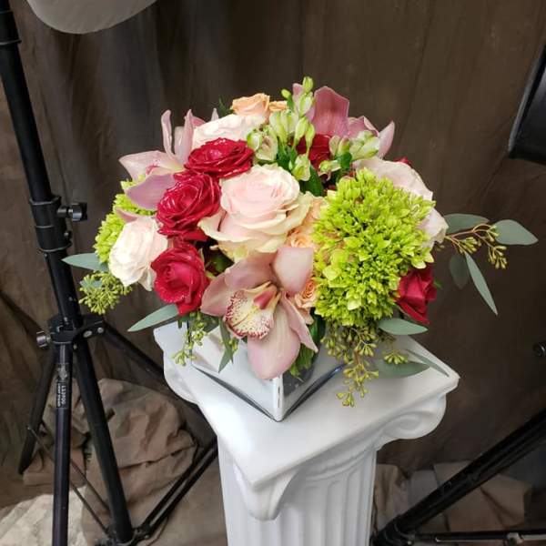 Bouquet of pink and red roses with orchids and green blooms in a white vase