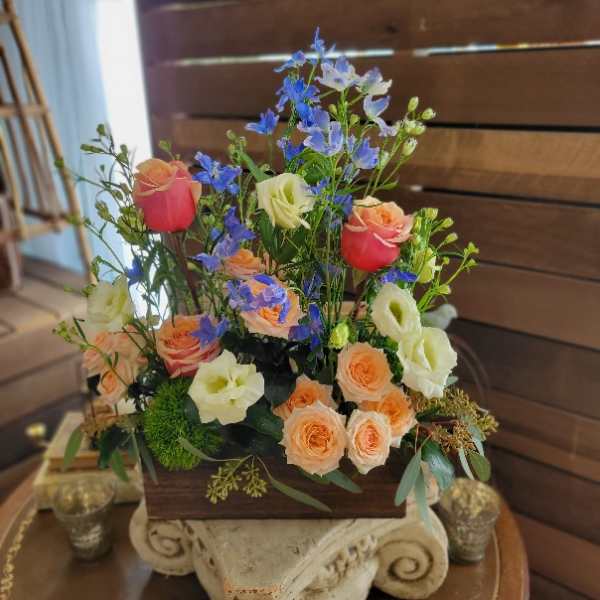 Mixed bouquet of peach, cream, and pink roses with blue filler flowers in a wooden box