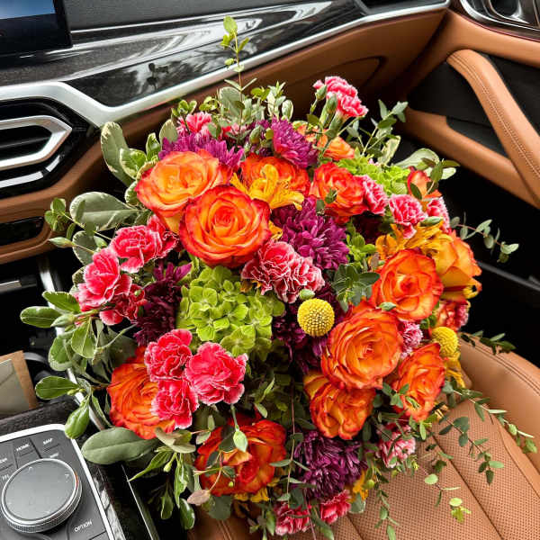 Bouquet of orange roses, pink carnations, and purple flowers in a car seat