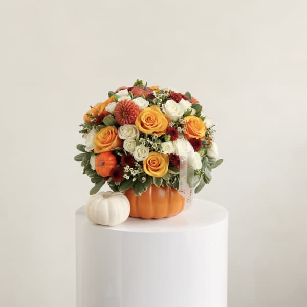 Orange and white flower arrangement in a pumpkin container with small pumpkins