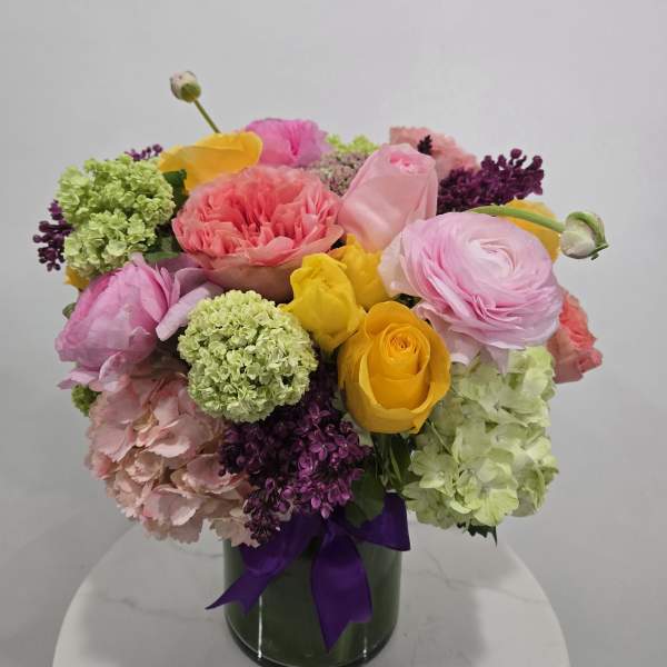 Colorful bouquet of roses and ranunculus in a glass vase with a purple ribbon