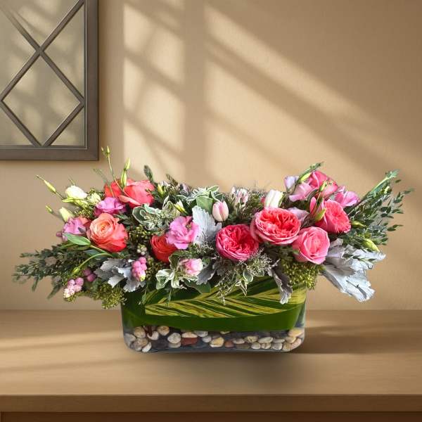 Pink and peach roses arranged in a low glass vase with stones