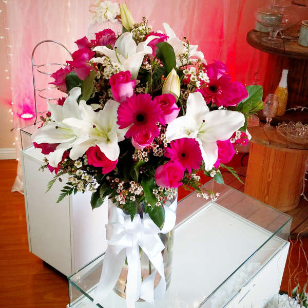 Pink and white mixed flower arrangement in a clear vase with a white ribbon