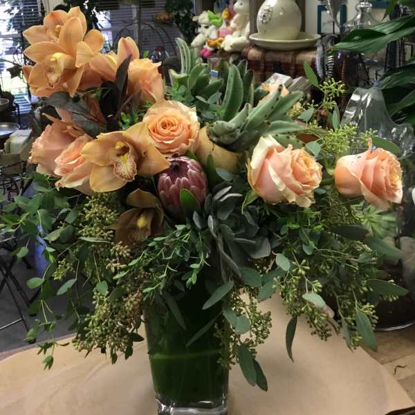 Peach roses and orchids in a glass vase with lush greenery
