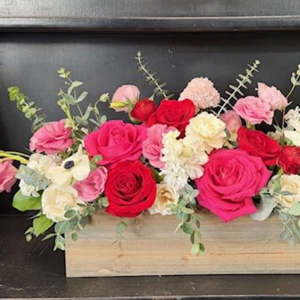Pink and red roses arranged in a wooden box with white flowers