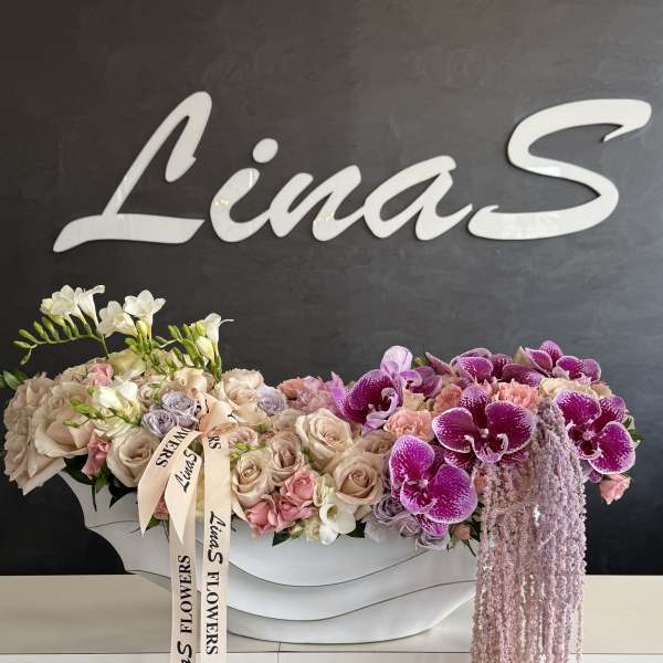 Large floral arrangement with pink roses and purple orchids in a white container