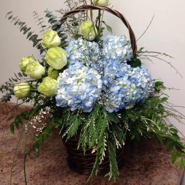 Basket arrangement with blue hydrangeas and pale green roses