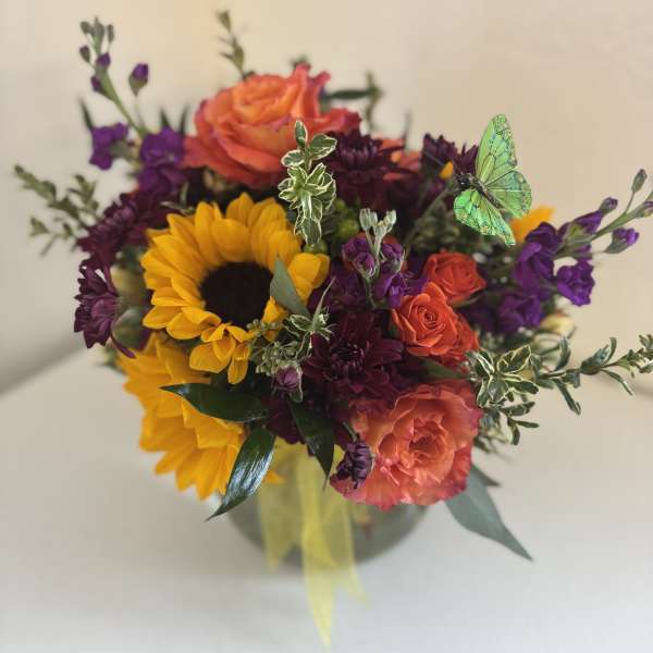 Bouquet of sunflowers, orange roses, and purple flowers in a vase