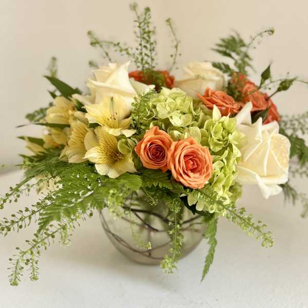Mixed bouquet of roses, hydrangeas, and pale yellow flowers in a glass bowl vase