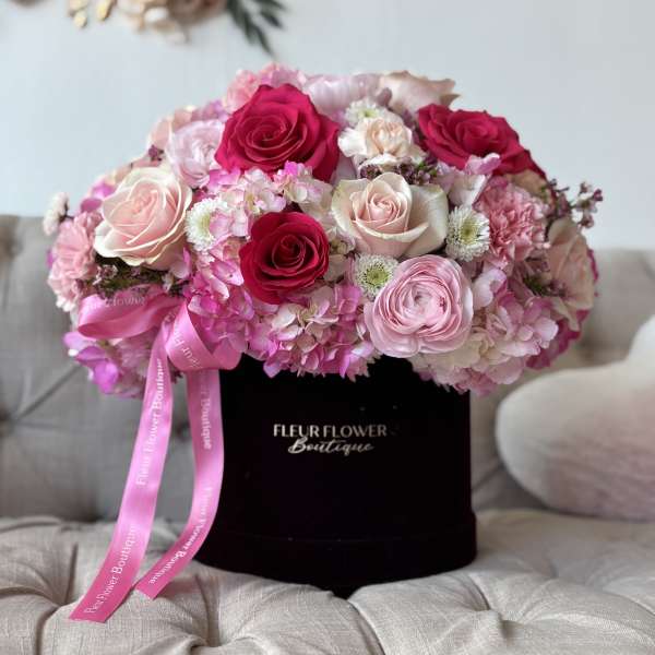 Pink and white rose bouquet in a black hat box with a ribbon