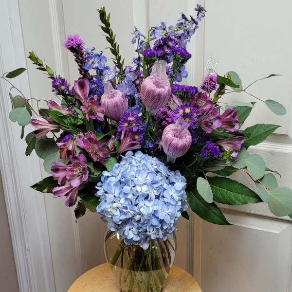 Bouquet of blue hydrangea, purple flowers, and pink alstroemeria in a glass vase