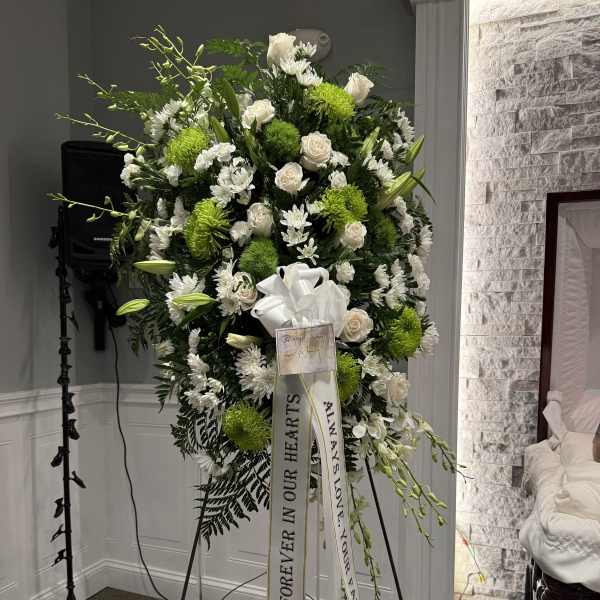 Standing sympathy spray of white and green flowers on an easel with ribbons