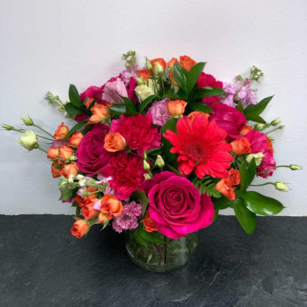 Mixed bouquet of pink, orange, and red flowers in a glass vase