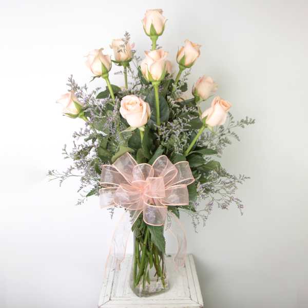 Bouquet of pale pink roses in a clear glass vase with a pink ribbon