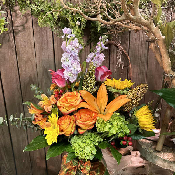 Mixed bouquet in a glass vase with orange roses, yellow daisies, and lavender spikes