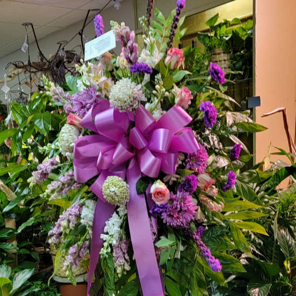 Large purple and pink floral standing spray with a ribbon bow