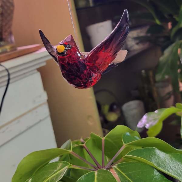Red glass bird ornament hanging above a green potted plant