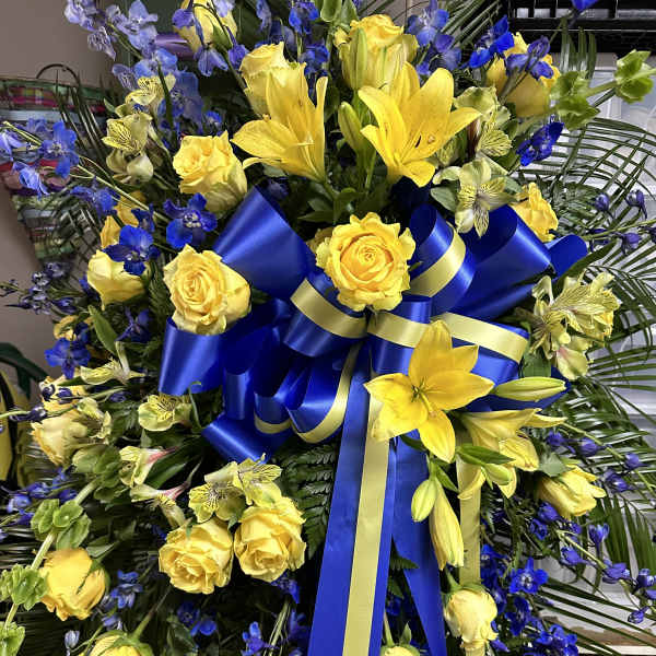 Yellow roses and lilies with blue flowers and a blue ribbon