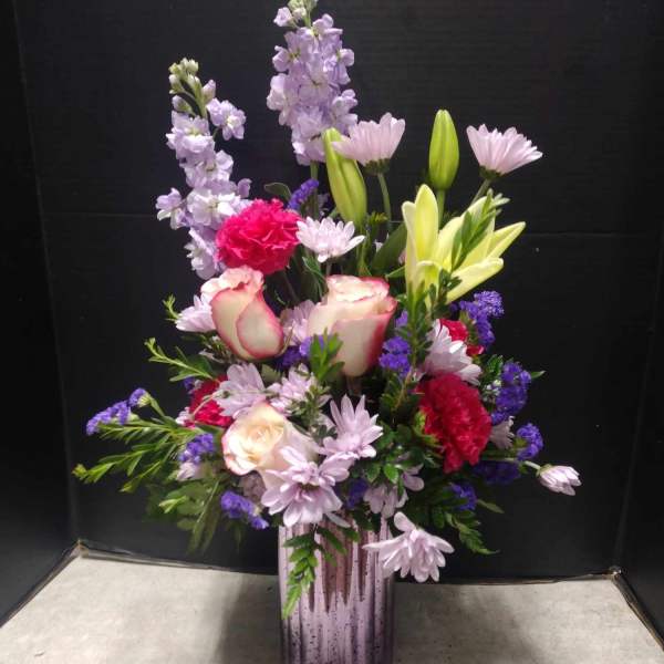 Mixed bouquet in a purple vase with pink, lavender, and yellow flowers