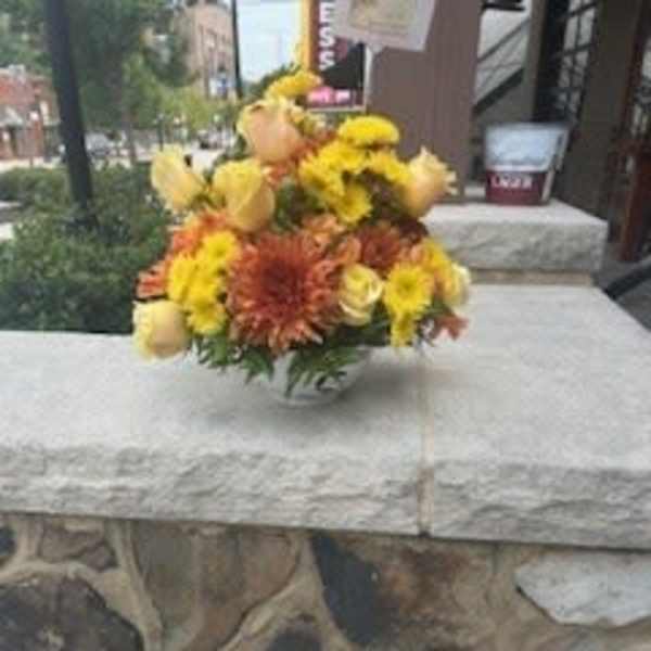 Yellow and orange flower arrangement in a clear vase on a stone table