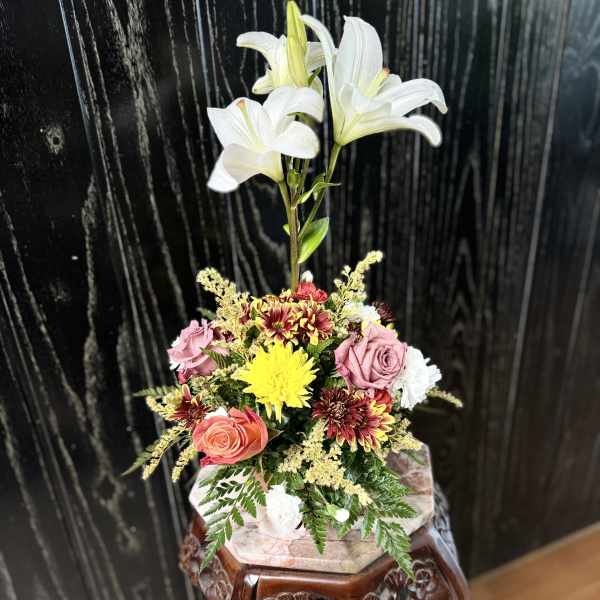 Arrangement of white lilies, roses, and chrysanthemums in a decorative container