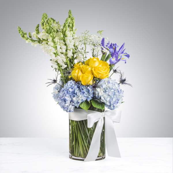 Bouquet of yellow roses, blue hydrangeas, and purple irises in a glass vase