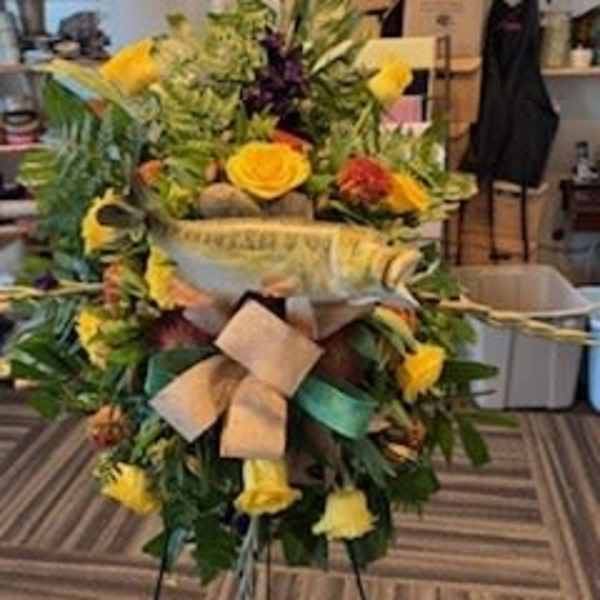 Large standing floral spray with yellow roses and greenery on a ribboned easel.