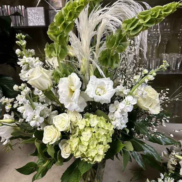 Tall white floral arrangement with green accents in a clear vase