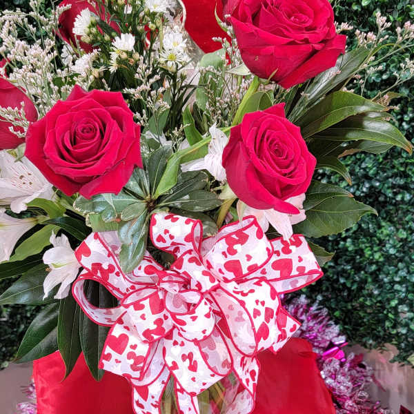 Bouquet of red roses and white daisies in a glass vase with a heart ribbon