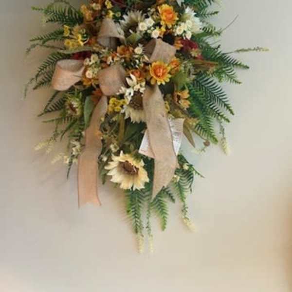 Wall-mounted floral spray with sunflowers, white blooms, and beige ribbons