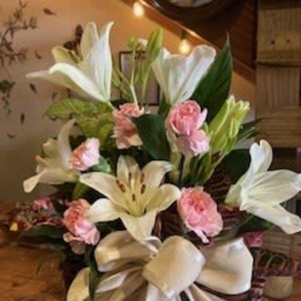 White lilies and pink carnations arranged with a large satin bow